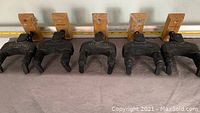 Five Hercules guitar hangers laid out in a row, showing the wooden mounting plates and black locking yokes