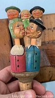 Close-up of the kissing couple wine cork showing hand carved and painted wood heads with a wooden mechanism for movement, featuring a woman in red with green hat and a man in blue with black hat.