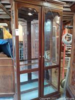 Front view showing wood framed double glass doors with glass shelves and mirrored back inside hutch.