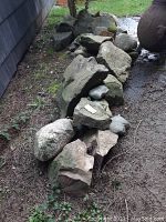 Photo showing a line-up of large and medium landscaping rocks outdoors on dirt ground; rocks vary from flat to rounded shapes, colors mostly gray tones.
