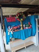 Wide view of the lot showing Christmas wreath, boxes, ribbons, tablecloths on blue background fabric