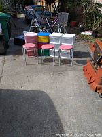 Overall view of four plastic storage bins and three pink stools arranged outdoors on pavement, showing size and color variety.