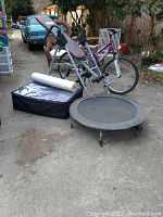 Overall lot showing Body Champ inversion table, personal trampoline, exercise mats in carrying case, foam roller, and Huffy mountain bike.