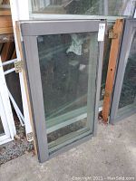 Two skylight windows leaning vertically against a wall, with wooden outer frames and gray inner trim, showing some dirt and dust on glass.