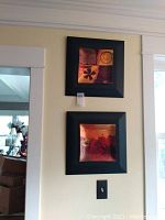 Two square framed pieces of wall art mounted vertically on a pale yellow wall, showing floral and abstract designs in warm tones.