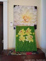 Two floral canvas paintings displayed vertically, white flower on top and yellow daffodils below