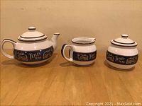 Photo showing Tetley Teas ceramic teapot, creamer, and sugar pot on a wooden surface.