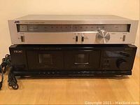 Photo of silver JVC T-V3 AM/FM tuner stacked on black TEAC W-420C stereo double cassette deck on a wooden surface.