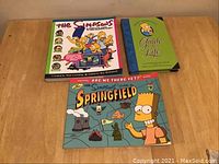 Three Simpsons books with colorful cartoon covers featuring main characters, arranged on table.