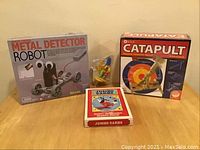 Overview of all items in the lot showing boxes of Metal Detector Robot kit, Catapult kit, Mickey Mouse jumbo playing cards, and a Simpsons figurine in front