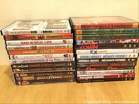 Photo of 26 DVDs and CDs stacked in two piles showing titles of movies, comedy specials, and music albums.