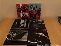 Photo showing two U2 05 Vertigo DVD sets with four separate U2 vinyl singles in black and white sleeves laid out on a table.