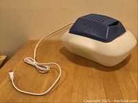 White and blue Sunbeam humidifier placed on wooden surface with power cord.