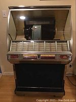 Full front view of jukebox on wood floor showing cabinet and visible record mechanism