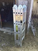 Ladder folded in vertical position resting against shed, showing aluminum frame and hinge locks