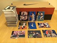 Stack of sports cards alongside Nike shoebox and a selection of baseball cards laid out on table showing player action shots.