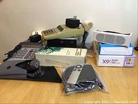 Overview of lot showing Apple TV 2nd generation with remote, Philips razor, Casio calculator missing feed roller, power adapters, and other electronics on wooden table.