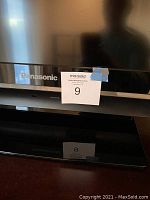 Close-up of Panasonic logo and base with auction number attached to TV.