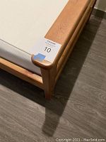 Close-up of pine wood bed frame corner showing tag and wood grain.