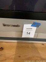 Close-up of the Panasonic brand name on the front lower bezel of the TV with the MaxSold auction tag number 14.