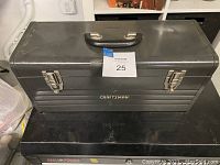 Closed gray Craftsman steel toolbox with handle and latches on a black surface.