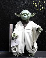 Front view of Yoda action figure standing next to a ruler showing 18 inches tall. Wearing cream robe and brown tunic. Green face with large ears.