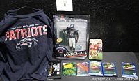 Full lot displayed showing the New England Patriots child's long sleeve T-shirt, Brandon Marshall action figure in original packaging, stack of trading cards in various packages and loose.