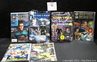 Lot of Playmates Star Trek action figures and comic books all displayed together on flat black surface. Items include vintage sealed figures of Doctor Bashir and Lt. Commander Data in prominently visible original packaging. Four Star Trek comic books visible with covers facing forward.