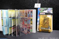 Open binder displaying colorful MLB trading cards in plastic sleeves alongside Sammy Sosa action figure in packaging.