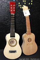 Overall view of two ukuleles: autographed 6-string Bridgecraft USA ukulele with strings and tuning pegs, and unfinished 4-string ukulele body without strings.
