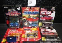 Lot includes six vintage die-cast replica cars in original packages representing muscle cars, racing champions, hot rods, and stock rods with some including stands and trading cards.
