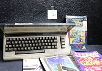 Front angled view of Commodore 64 computer unit with keyboard and dust cover. Surrounding the unit are various manuals and software packaging including '35 Games' and 'The Speed Rumbler'.
