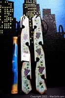 Photo showing the blue bamboo rainstick featuring hand-painted dolphins and ocean detail beside two wooden hanging grapevine holders hand-painted with purple grapes and green leaves.