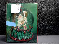 XL Holiday water globe inside original packaging, showing green box with festive Santa Claus and holly design.