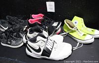 Photo showing 5 pairs of children's sneakers including black and pink Air Jordans, black and white Nike Velcro and lace-up sneakers, fluorescent yellow Converse All-Stars, and black DC Shoe Co hi-tops arranged on black surface.