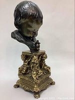 Front angled view of the child's bust sculpture showing the detailed brass cherub base and the child's head looking down.