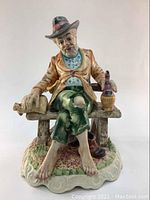 Front view of the Capodimonte porcelain tramp figurine sitting on a bench, showing detailed paint on face, clothing and shoes around the bench base.