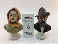 Two porcelain busts of an elderly woman and man displayed side by side on white bases.
