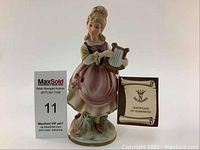 Front view of Capodimonte girl playing harp porcelain figurine with certificate of guarantee tag attached and auction label.