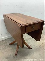 Side view showing one drop leaf folded down and the drawer on the table end.