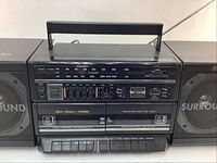 Front view of the Fisher boombox showing the tuning dial, dual cassette decks, equalizer sliders, control buttons, and label details.