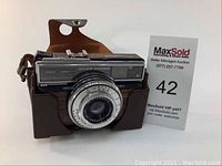 Front and side view of the vintage Voigtlander Vitessa 500AE camera inside its case, showing wood veneer and lens detail.