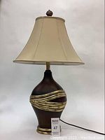Full view of the vintage table lamp showing the beige shade, tapered bronze body with gold bands, and finial.