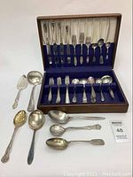 Full view of the cutlery set inside the wooden box plus additional serving utensils laid out in front, showing the mismatched pieces and box condition.