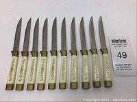 Full set of 10 vintage Korium steak knives with ivory-colored handles and gold floral design.