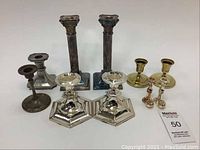 Overall view of the lot of nine candle sticks showing different styles and materials including silver plate and brass.