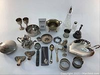 Full lot overview on white background showing all silver plated items laid out including dishes, spoons, teapot, goblets, decanter, pepper grinder, and other small pieces.