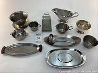 Photo showing entire set of twelve stainless steel items including trays, bowls, cups, napkin holder, gravy boat, and serving spoon arranged on white surface.
