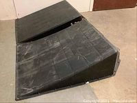 Image shows one black plastic ramp from a side angle with visible scratches and cracks
