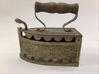 Side view showing ornate floral and scroll embossing on brass coal iron body and wooden handle with metal supports.